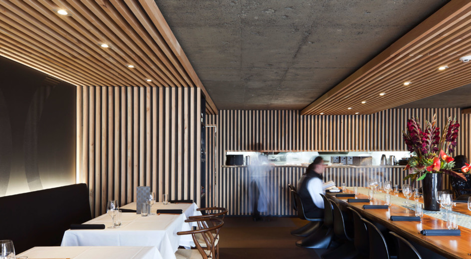 Cafe Seating Layout: Transforming Guest Experience 1 Restaurant interior with a long shared dining table, timber slatted ceiling and black banquette seating along the wall