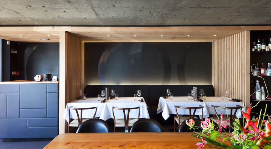 Cafe Seating Layout: Transforming Guest Experience 2 Restaurant dining area with white-clothed tables, wooden chairs and upholstered banquette under a timber and concrete ceiling