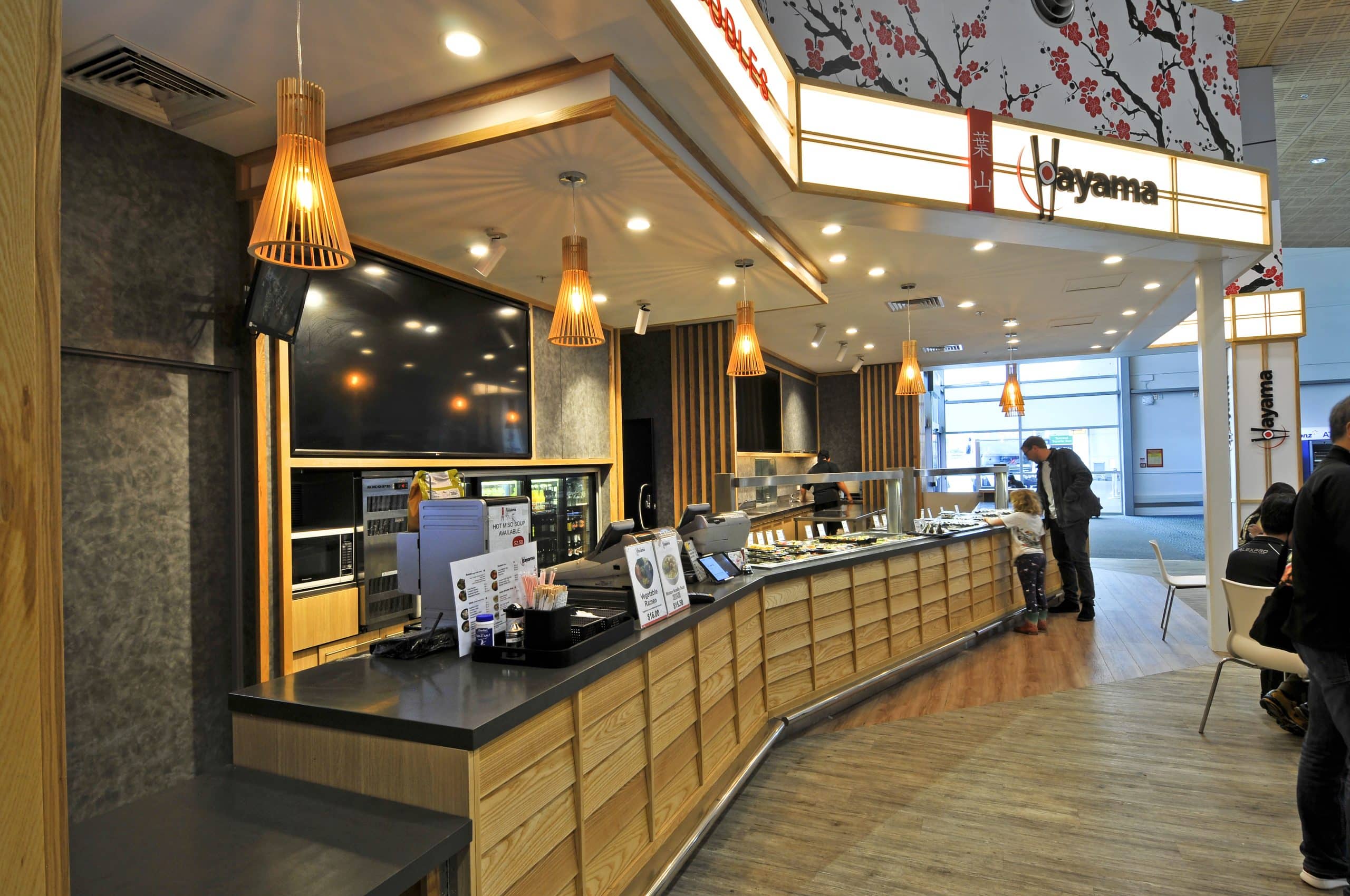Hayama sushi counter at Auckland Domestic Airport with an illuminated bulkhead and timber pendant lights